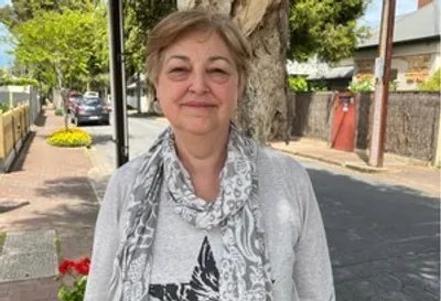 Smiling person on a sunny street, wearing a grey cardigan and a patterned scarf.