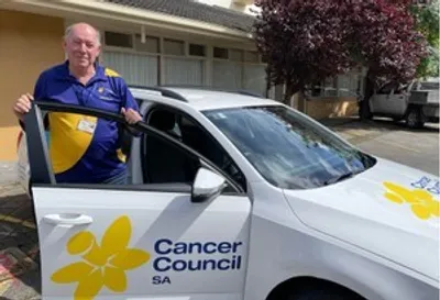 Person standing beside a white Cancer Council SA car with a yellow flower logo, giving thumbs up
