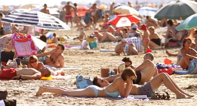 Bustling beach scene with many sunbathers on the sand beneath colourful umbrellas.