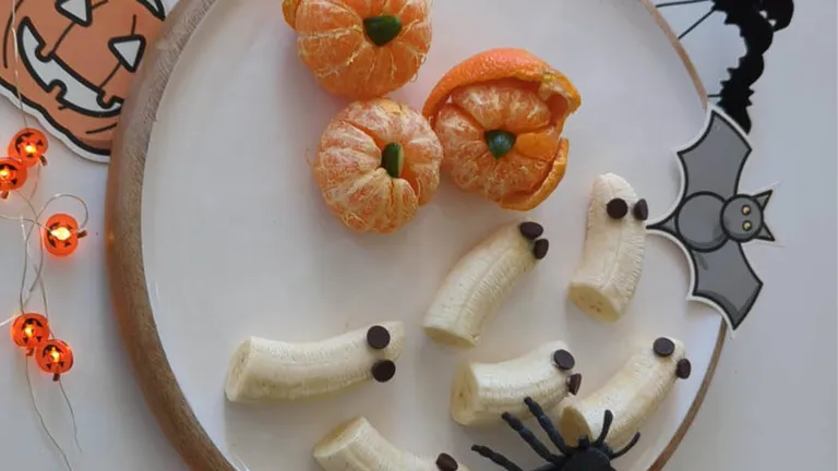 Halloween-themed plate with banana ghosts, pumpkin-shaped mandarins, and a black spider decoration.