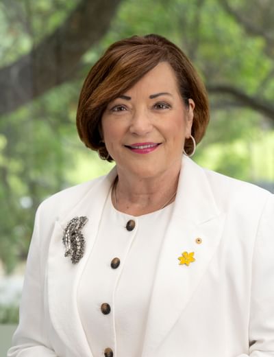 Portrait of a person with short brown hair, hoop earrings, wearing a white blazer, smiling.