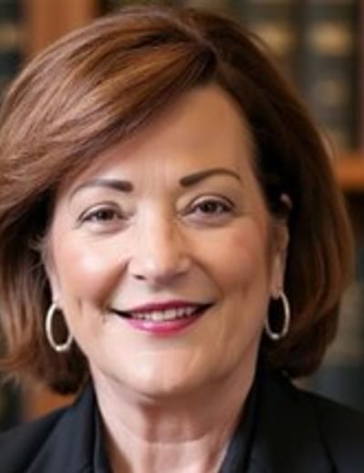 Portrait of a person with short brown hair, hoop earrings, wearing a black blazer, smiling, library.