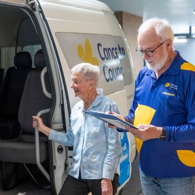 An elderly person steps into a Cancer Council van as a volunteer takes notes on a clipboard.