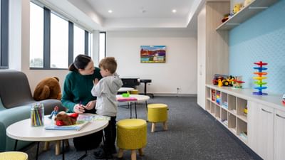 Adult and child at a round table with colouring and toys in a bright playroom.