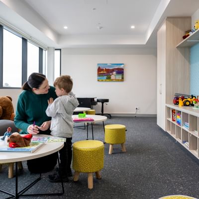 Adult and child at a round table with colouring and toys in a bright playroom.