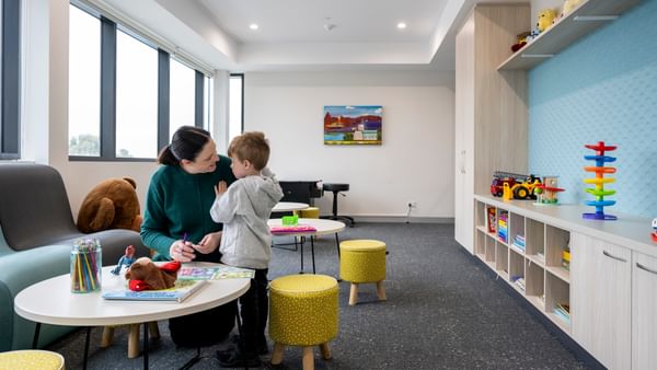 Adult and child at a round table with colouring and toys in a bright playroom.