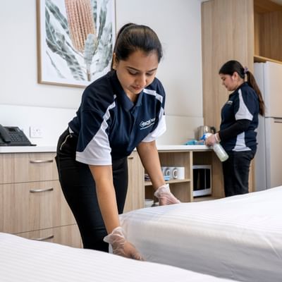 Two house keeping staff cleaning and making the bed in a hotel room.