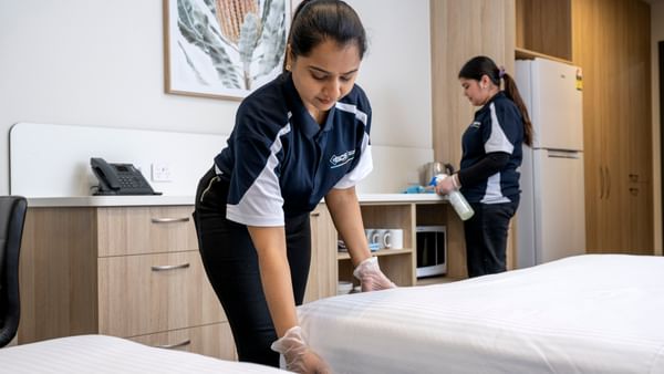 Two house keeping staff cleaning and making the bed in a hotel room.