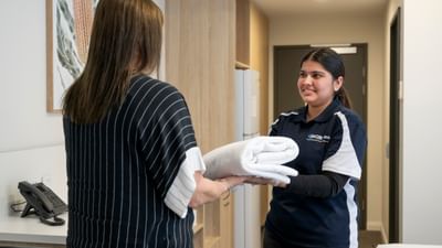 A staff member hands a folded white towel to a smiling visitor in a bright, modern clinic.