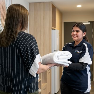 A staff member hands a folded white towel to a smiling visitor in a bright, modern clinic.
