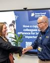 A man and a woman shake hands in front of a presentation screen