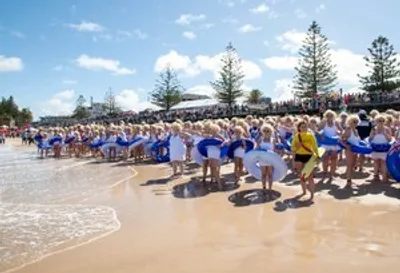 Group of people in blue outfits performing on a sunny beach, with one person in yellow.