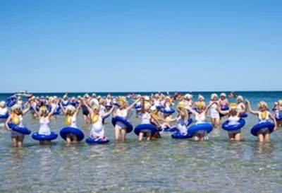 Group of people in swimsuits with inflatable rings in shallow beach water.