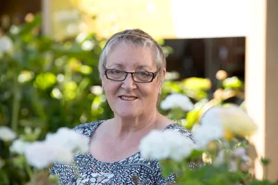 A close up of a woman smiling, in a garden surrounded by flowers.