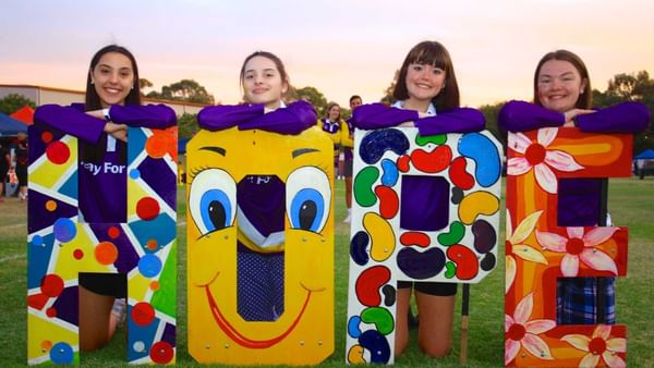 Four people lean on colorful painted letters spelling HOPE on a grassy field at sunset.