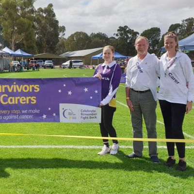 Four people on a grassy field hold a purple 'Survivors & Carers' banner at a cancer charity event.