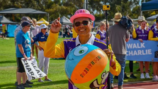 Smiling person in yellow and purple holds a beach ball on a selfie stick at a charity walk.