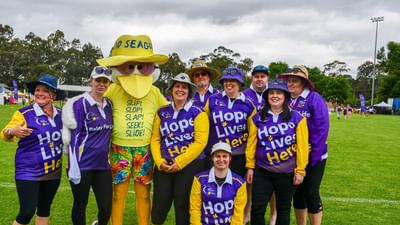 Group of people in purple Hope Lives Here shirts posing with a yellow seagull mascot on a field.