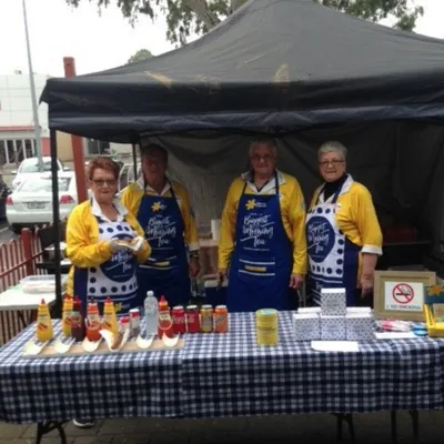 Four people in yellow shirts and blue aprons behind a condiment stall at an outdoor event.