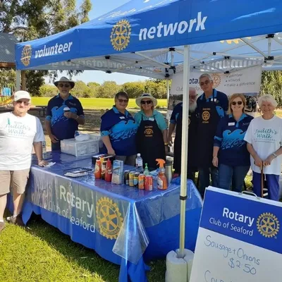 Group of volunteers at a Rotary Club stall under a blue canopy in a park.