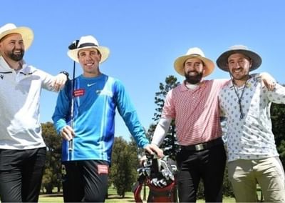 Four people in sun hats pose with golf clubs on a sunny golf course.
