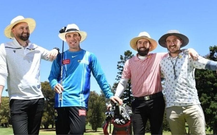 Four people in sun hats pose with golf clubs on a sunny golf course.