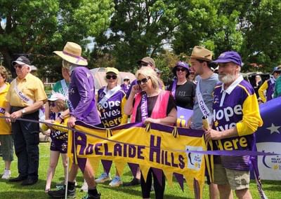 Group of people in purple and yellow hold an Adelaide Hills banner at a Relay For Life event.