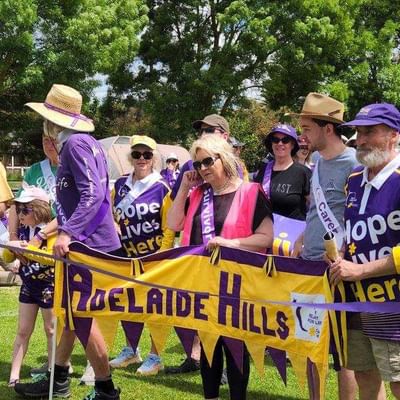 Group of people in purple and yellow hold an Adelaide Hills banner at a Relay For Life event.