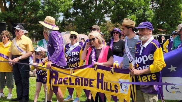 Group of people in purple and yellow hold an Adelaide Hills banner at a Relay For Life event.