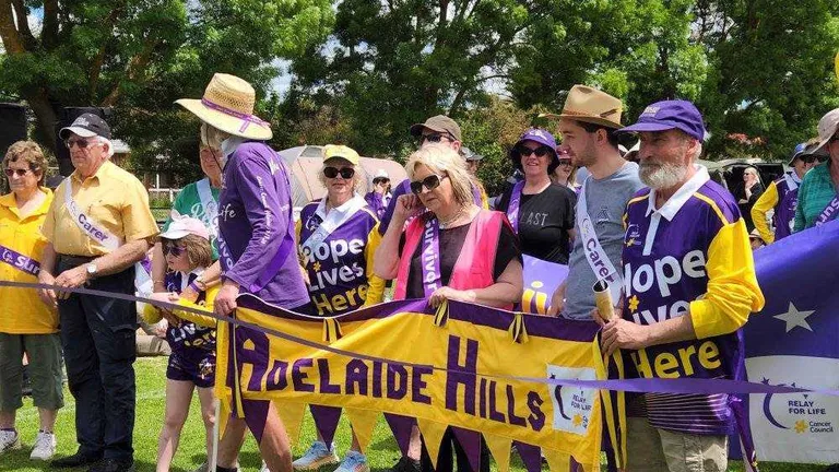 Group of people in purple and yellow hold an Adelaide Hills banner at a Relay For Life event.