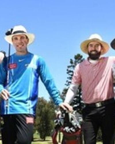 Four people wearing hats stand on a sunny golf course, smiling and posing with golf clubs.