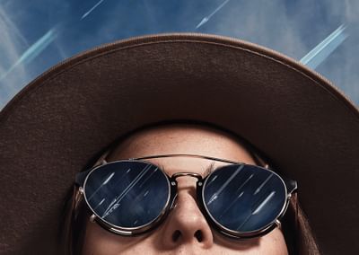 Woman looking up at sky, wearing hat and sunglasses. Sun rays represented as arrows.