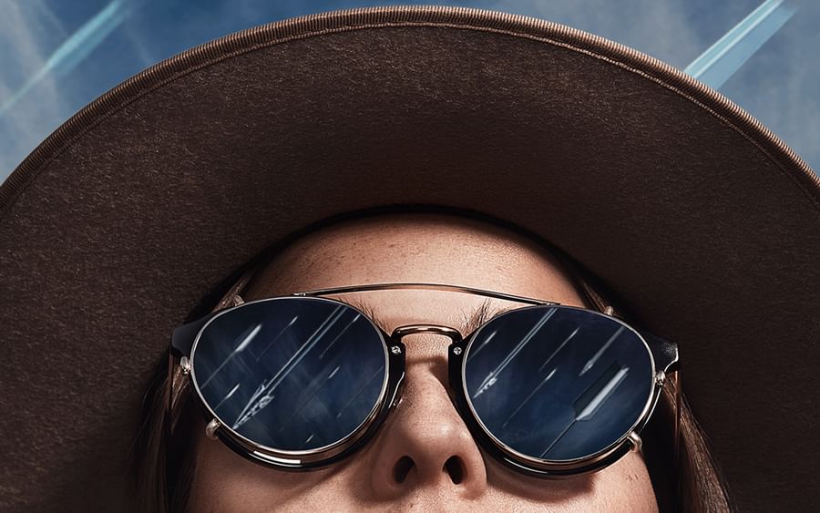 Woman looking up at sky, wearing hat and sunglasses. Sun rays represented as arrows.