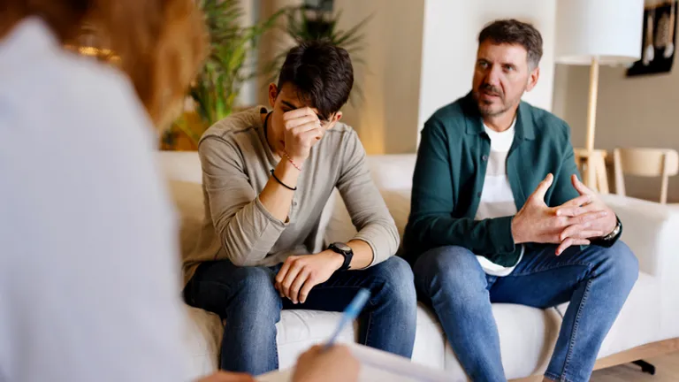 Two on a sofa; one distressed with a hand over their face, while another person takes notes.