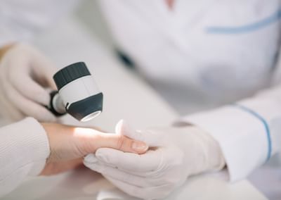 Close-up of a gloved clinician using a dermatoscope on a patient's fingertip.