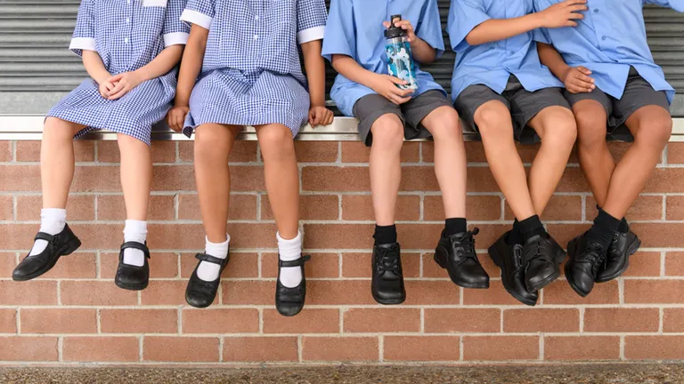 Group of students in blue uniforms sit on brick steps; one holds a water bottle.