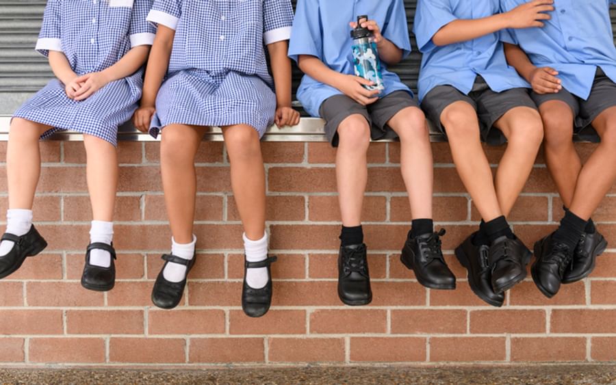 Group of students in blue uniforms sit on brick steps; one holds a water bottle.