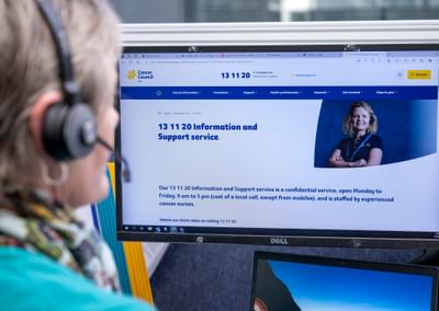 Person with headset viewing a monitor showing the Cancer Council SA Information and Support page.
