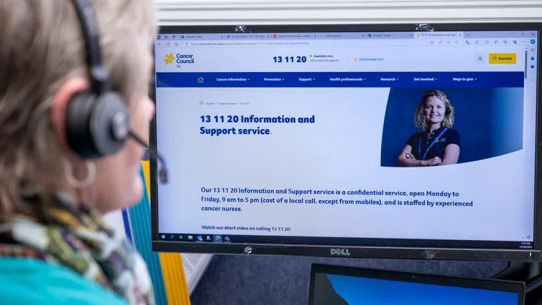 Person with headset viewing a monitor showing the Cancer Council SA Information and Support page.