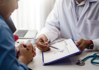 Doctor in a white coat explains a chart to a patient; stethoscope on the desk.