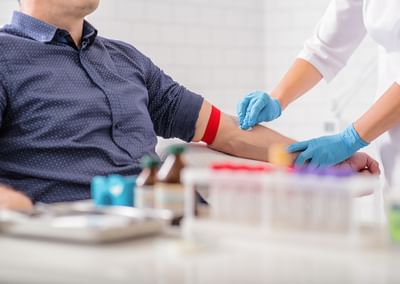 Medical professional wearing blue gloves draws blood from a patient’s arm with a red tourniquet.