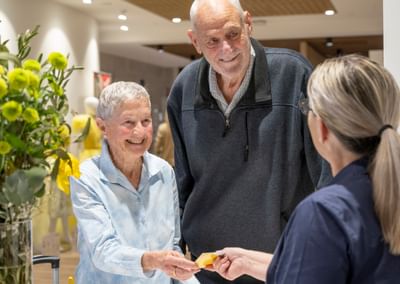 Smiling elderly couple exchange a yellow card with a staff member in a bright shop.
