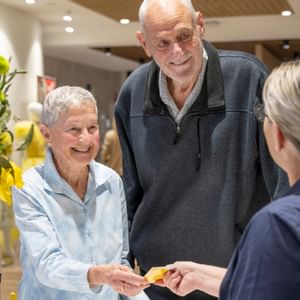 Smiling elderly couple exchange a yellow card with a staff member in a bright shop.