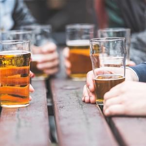 Several people hold pint glasses of beer at a wooden table.
