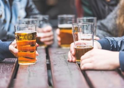 Several people hold pint glasses of beer at a wooden table.