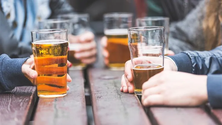 Several people hold pint glasses of beer at a wooden table.