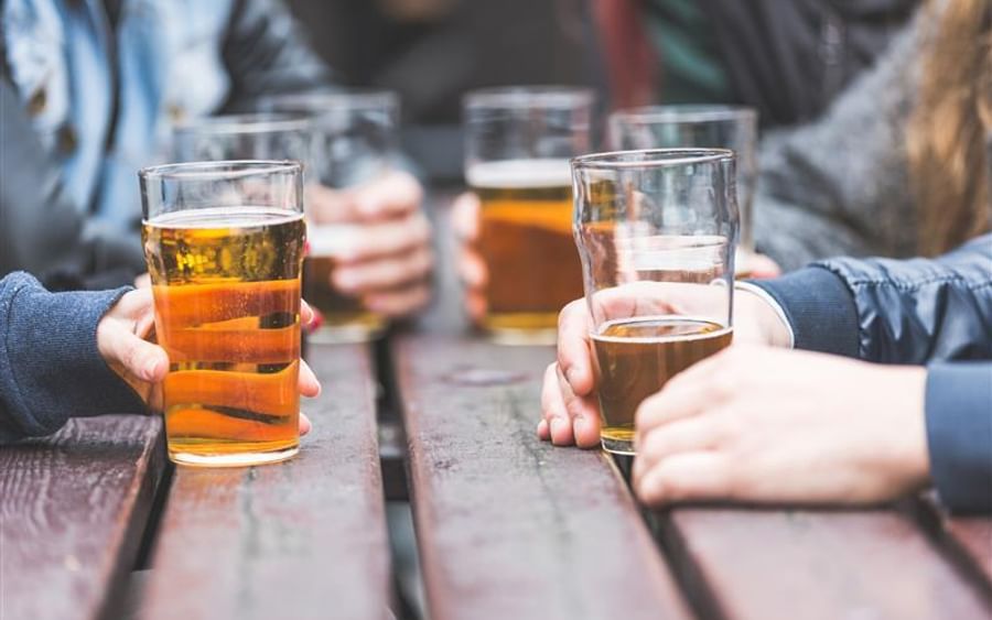 Several people hold pint glasses of beer at a wooden table.
