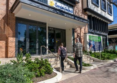 Two people walk up the steps to the Cancer Council entrance with glass doors and plants.