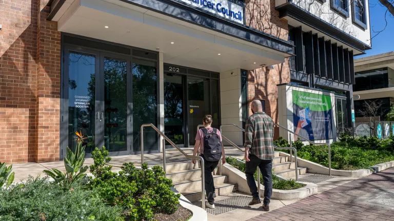 Two people walk up the steps to the Cancer Council entrance with glass doors and plants.