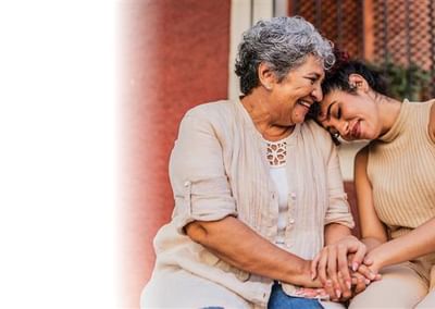 Two people outdoors, smiling and holding hands, one leaning on the other's shoulder.